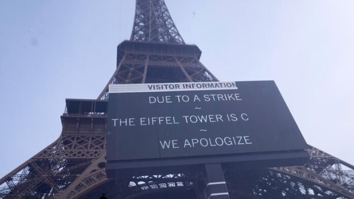 Protesters carrying CGT union flags march in Paris near the Eiffel Tower during nationwide strikes against austerity cuts on October 2, 2025